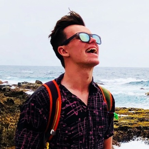 Alex standing on a beach wearing sunglasses.