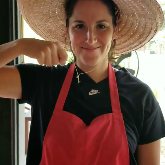 Ariana smiling and miming eating in a large straw hat.