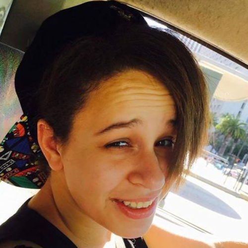 Elisa smiling at the camera with a creased brow in the driver's seat of a car.