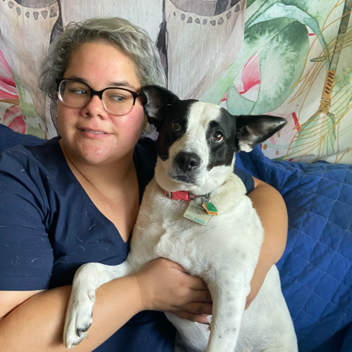 Krista on a couch holding a dog that is medium sized, white with large black ears.